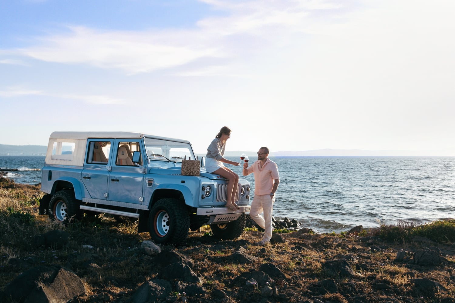 Restored Land Rover Defender D110 with custom modifications and modern upgrades. Bespoke Monarch Defender parked by the ocean with two people enjoying the view